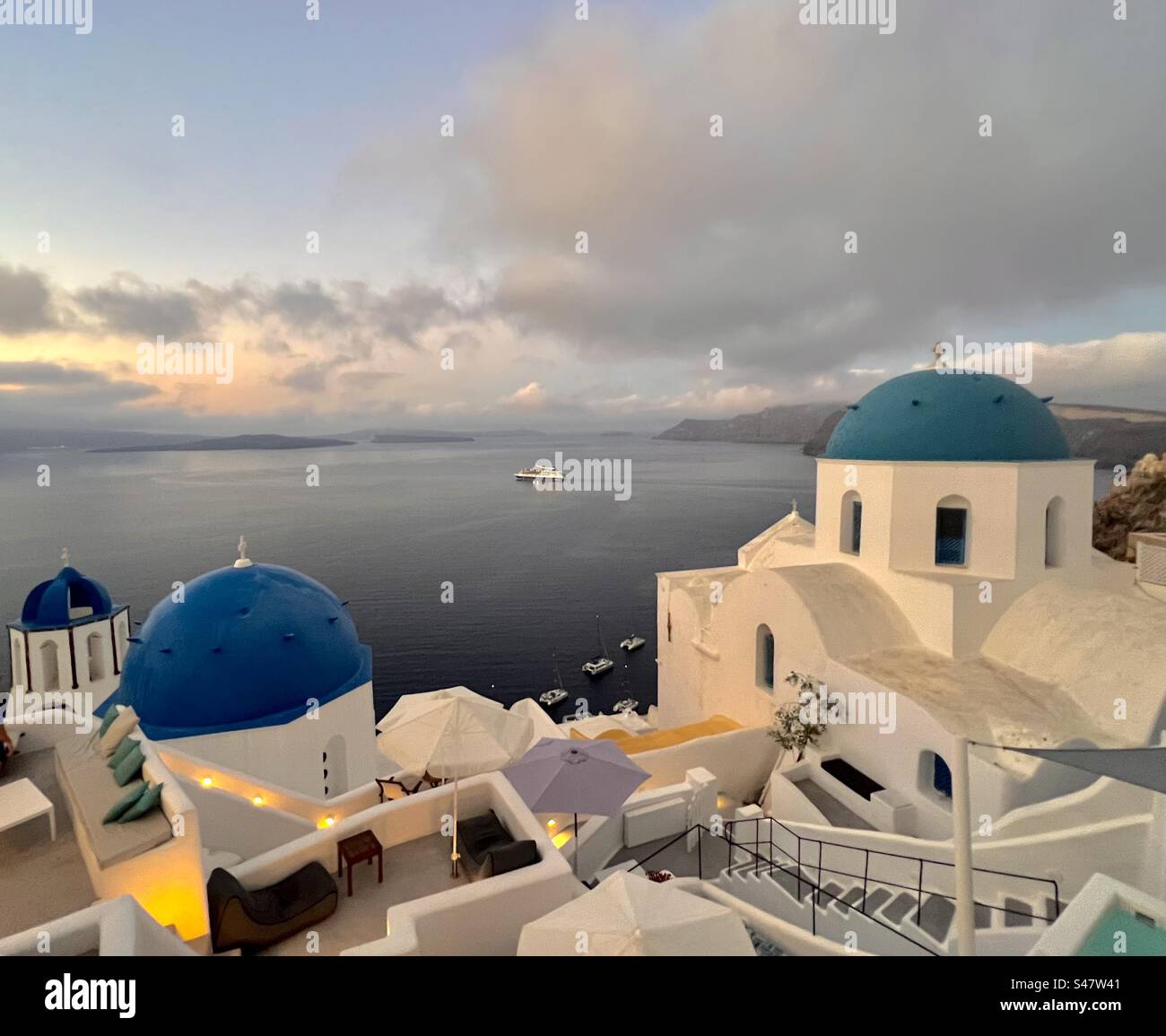 Le tre cupole blu e il bagliore dell'alba a Oia, Santorini - Immagine stock catturata con smartphone