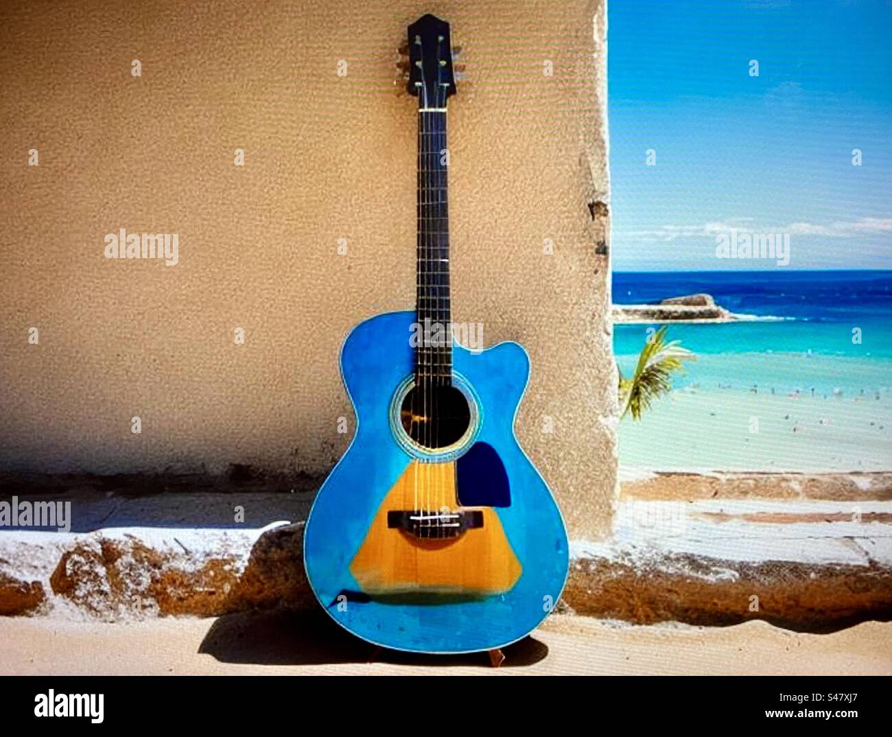 Chitarra blu addossata a un muro durante il sole estivo con il mare blu sullo sfondo Foto Stock