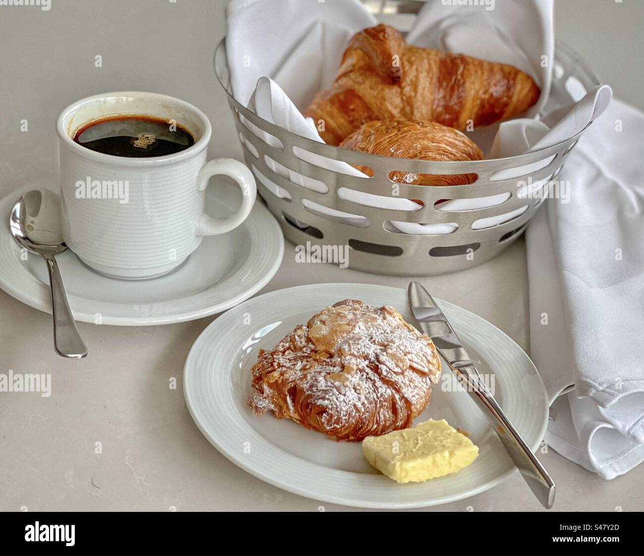 Vista dall'alto della colazione continentale: Croissant in ciotola metallica, pasticceria e burro sul piatto e una tazza di caffè nero. - Immagine stock catturata con smartphone