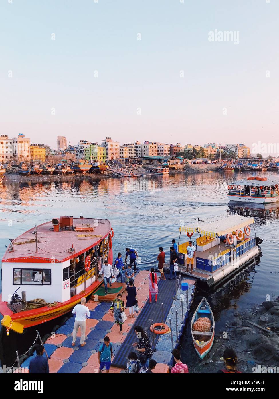 Un molo affollato a Mumbai con persone, barche e lanci con lo skyline sullo sfondo - Immagine stock catturata con smartphone