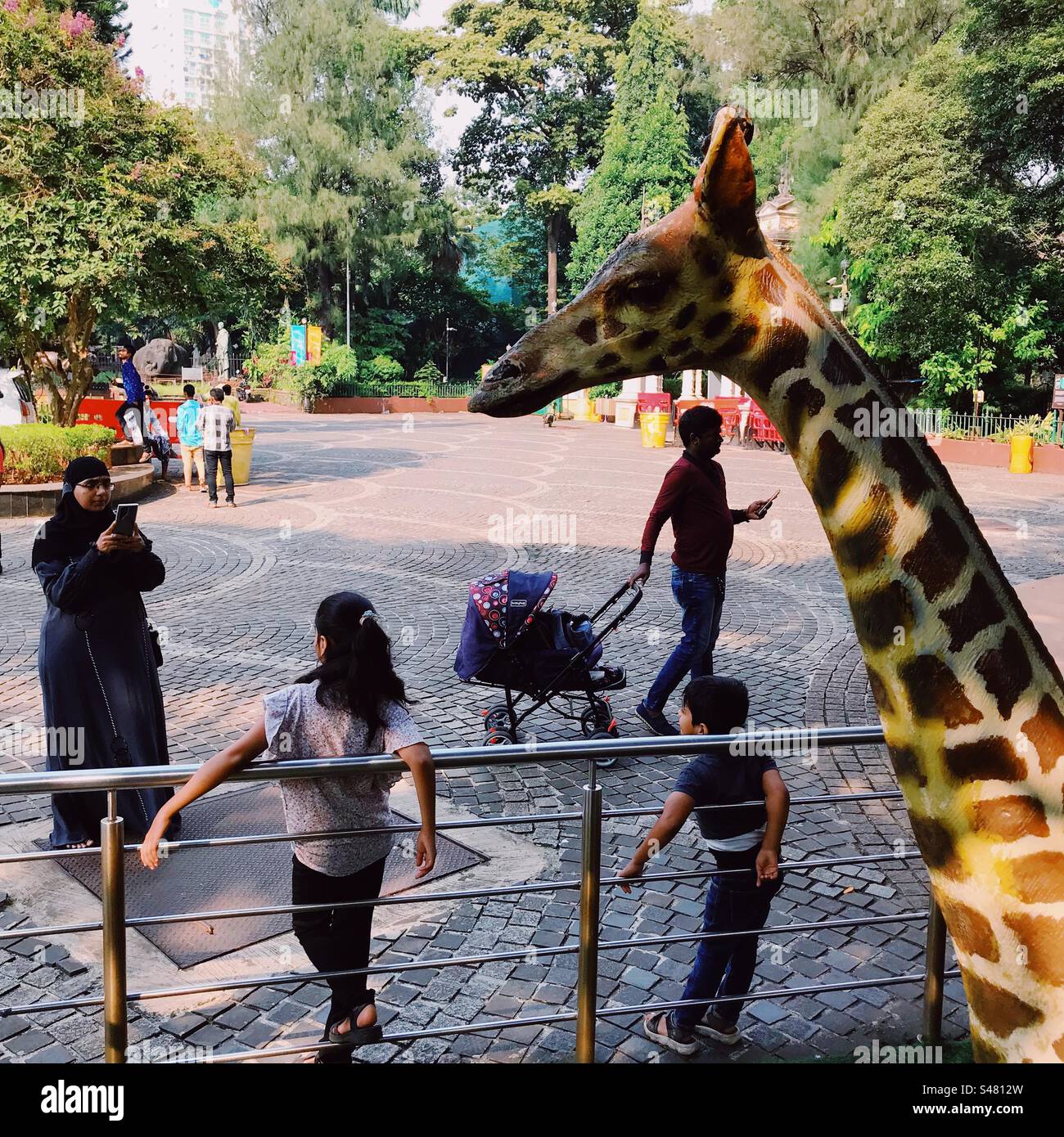 Una donna musulmana nel suo burka che scatta foto di bambini allo zoo di Mumbai - Immagine stock catturata con smartphone