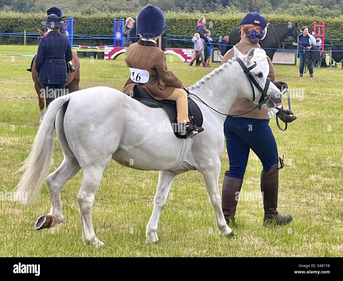 Un bambino piccolo cavalca un piccolo pony bianco su una pista in una campagna inglese gymkhana Foto Stock