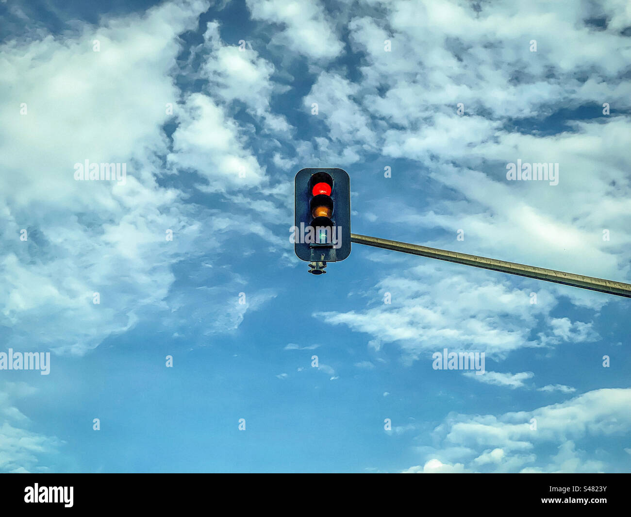 Vista angolare bassa della luce di stop rossa che si accende al semaforo contro il cielo blu con le nuvole. Foto Stock