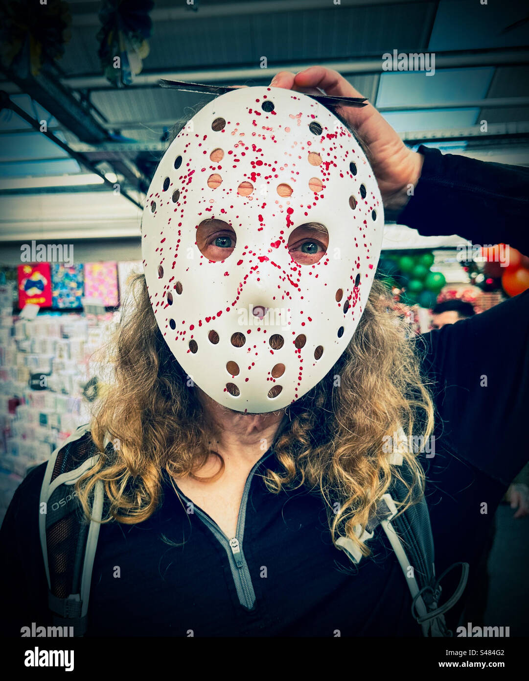 Un uomo prova una maschera spaventosa in un negozio per Halloween - Immagine stock catturata con smartphone
