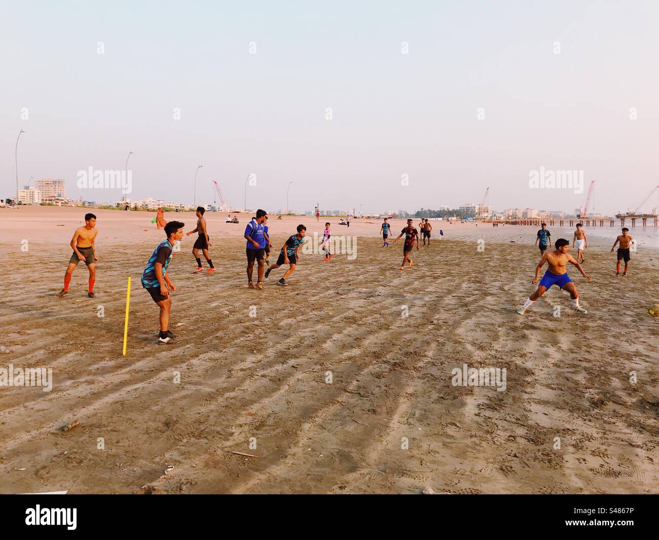 Giovani adulti che giocano a calcio o a calcio su una spiaggia con lo skyline di Mumbai sullo sfondo - Immagine stock catturata con smartphone