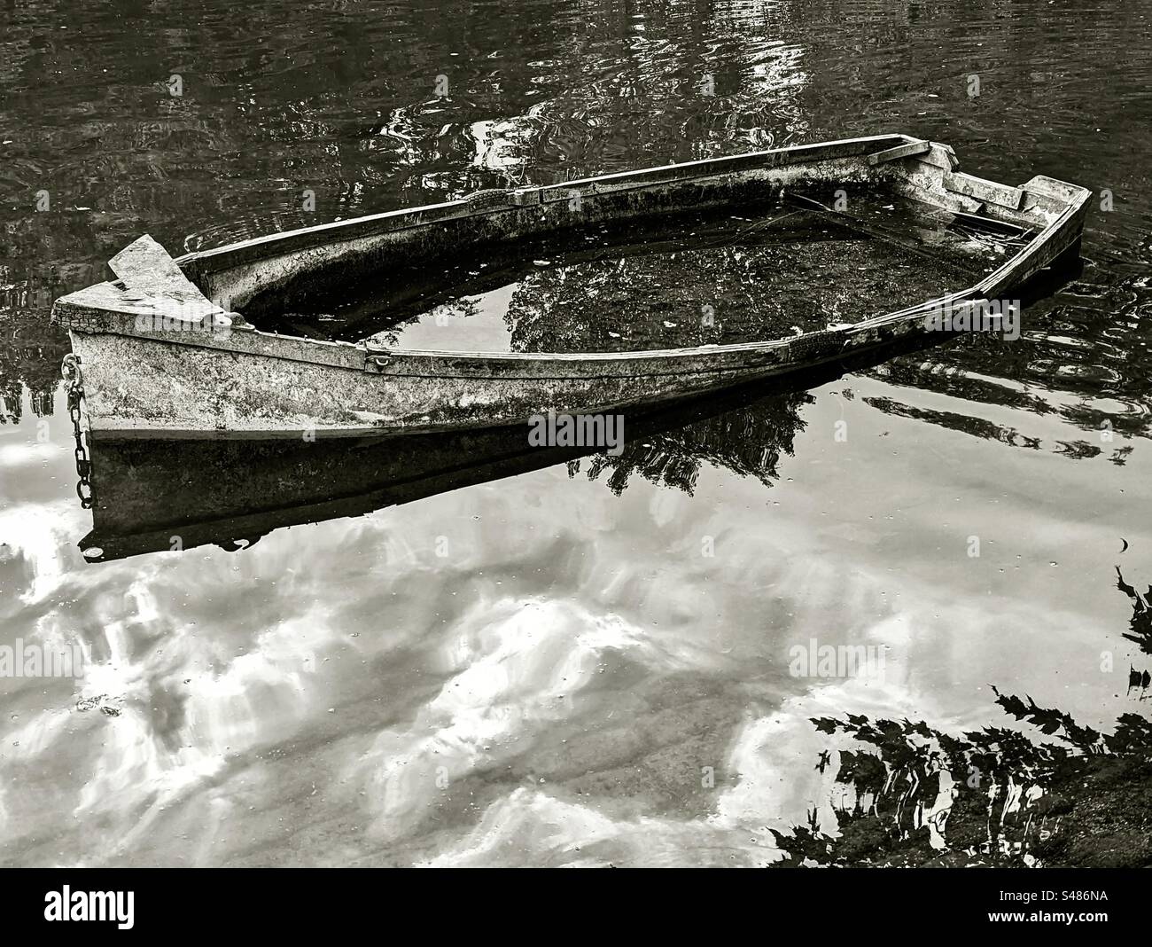 Una barca abbandonata piena d'acqua tra riflessi nuvolosi Foto Stock