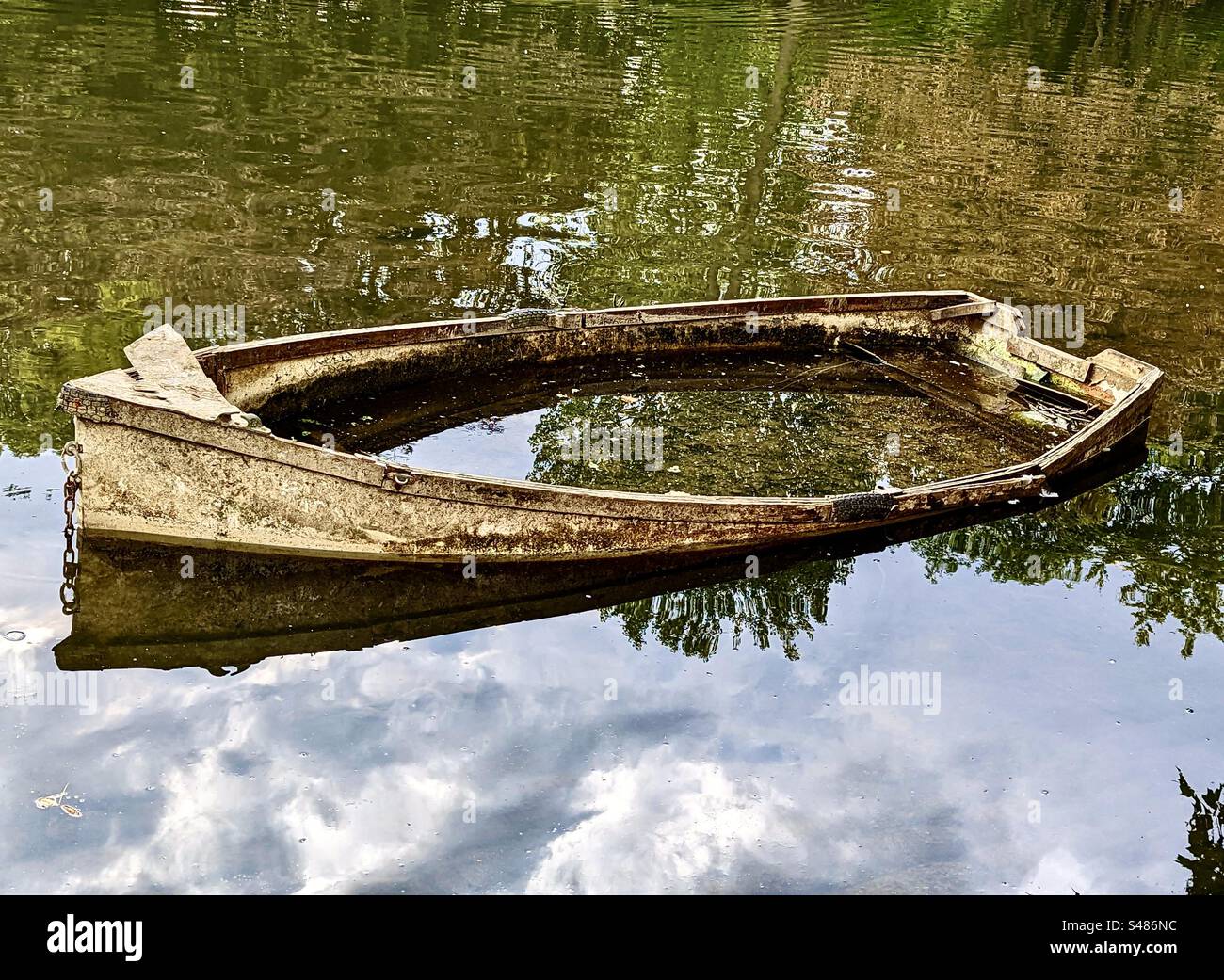 Una barca abbandonata piena d'acqua, tra riflessi nuvolosi Foto Stock