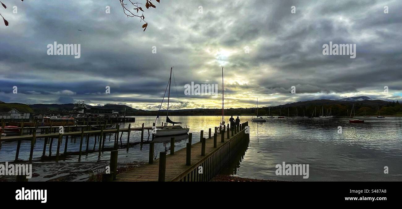 Guardando Windermere al crepuscolo da Waterhead, Ambleside con un paio di persone in piedi sul molo - Lake District Regno Unito Foto Stock