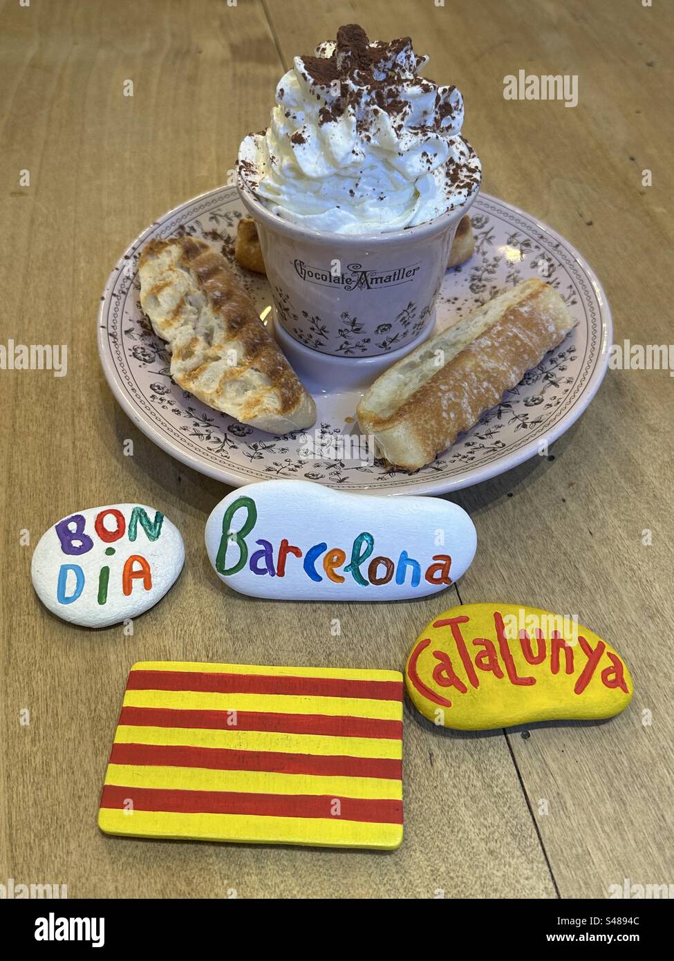 Colazione a Barcellona con cioccolata calda e panna, pane dolce e pietre dipinte e scolpite e bandiera catalana dipinta a mano su legno Foto Stock