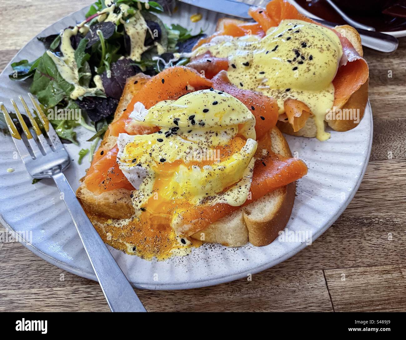 Primo piano di uova Benedict con salmone affumicato, salsa hollandaise e foglie di spinaci su shokupan/pane al latte giapponese su piatto sul tavolo. - Immagine stock catturata con smartphone