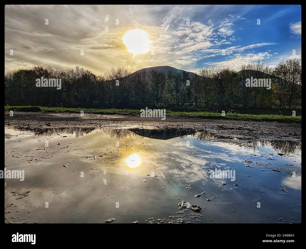 Le colline di Eildon si riflettono in una pozzanghera con il sole e il cielo blu. Foto Stock