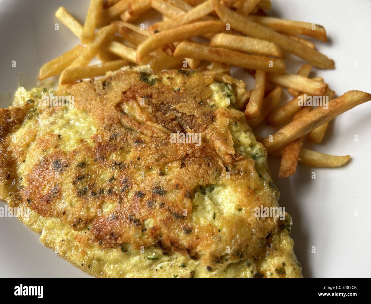 Omelette a base di formaggio ed erbe aromatiche, servita con croccanti patatine fritte dorate. Foto Stock