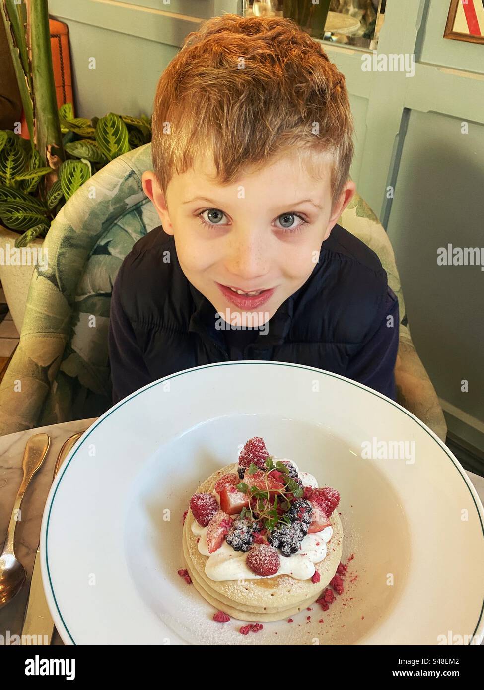 Bambino di sette anni con pancake al burro per colazione. Foto Stock