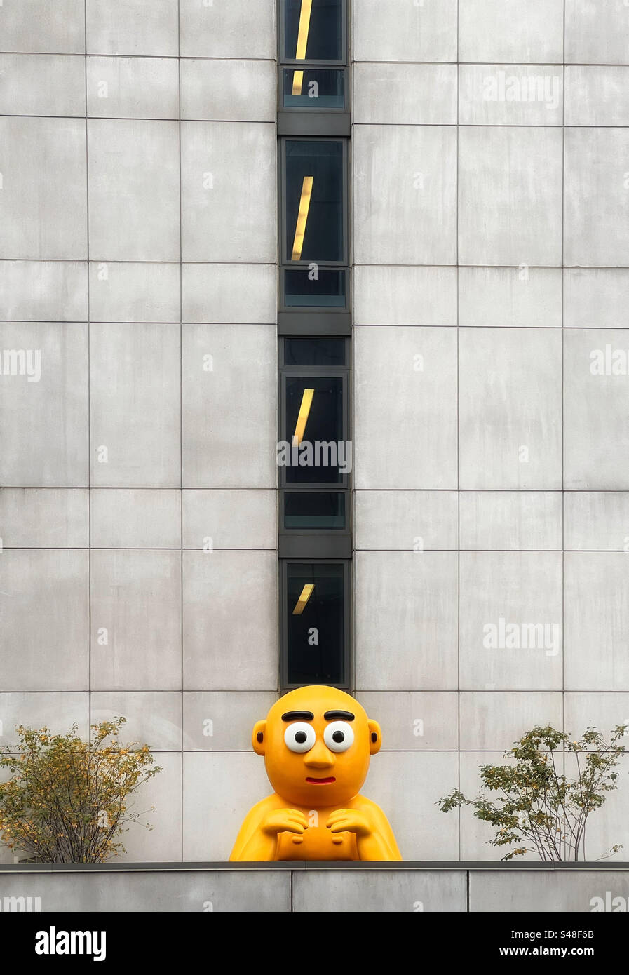 Personaggio simile a un cartone animato in giallo che sbircia su una parete di grattacielo sulla 30th Avenue, New York come visto dal giardino sopraelevato High Line Foto Stock