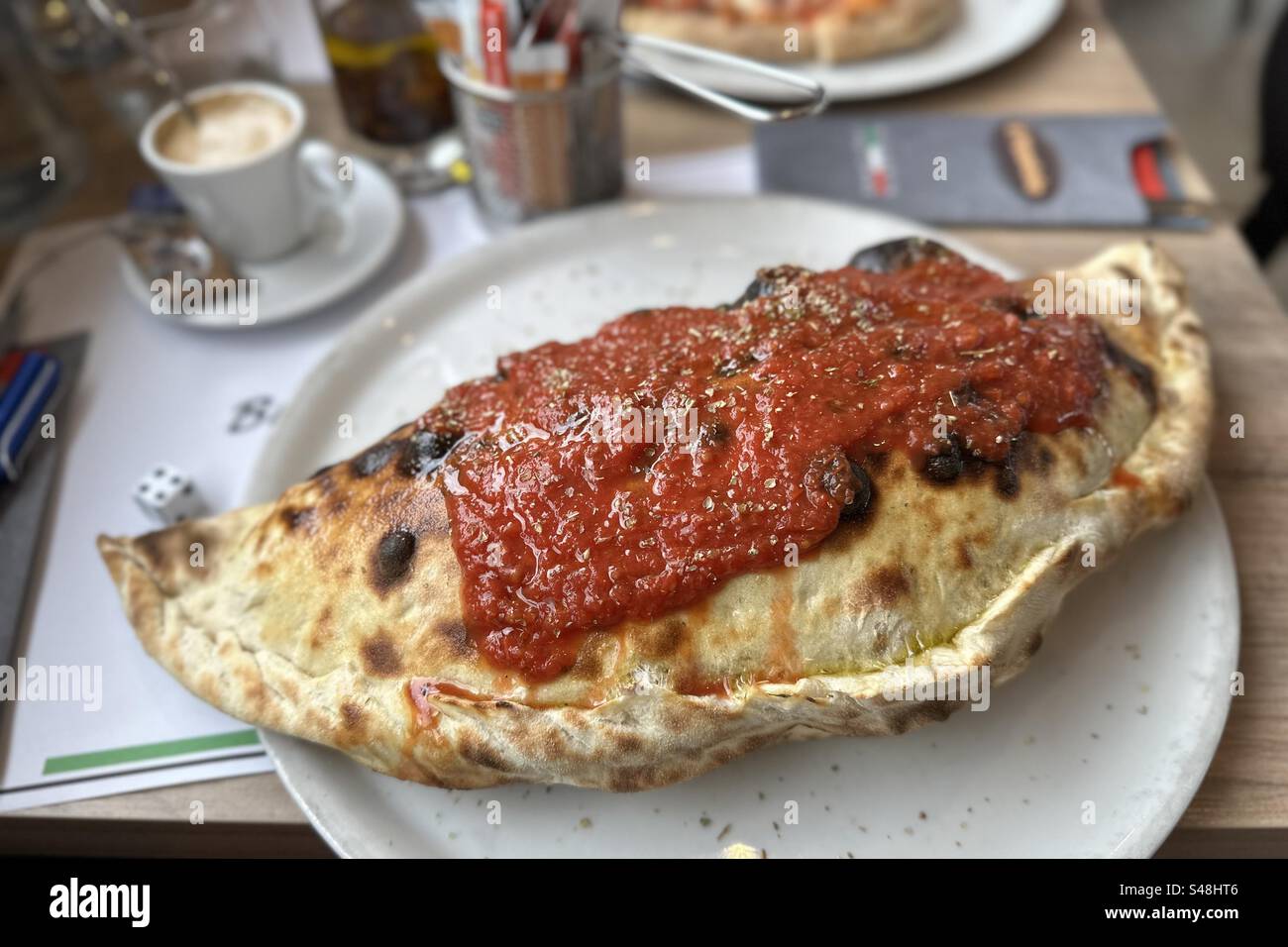 Pizza Big Calzone su un piatto bianco, condita con salsa di pomodoro bolonia - Immagine stock catturata con smartphone