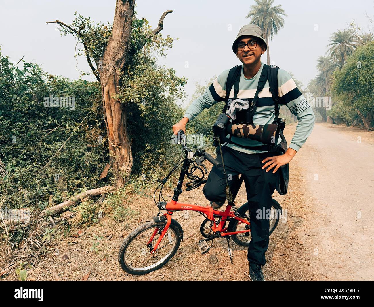 Un fotografo di fauna selvatica con la sua macchina fotografica e bicicletta pieghevole sorridente e in posa in una giungla Foto Stock