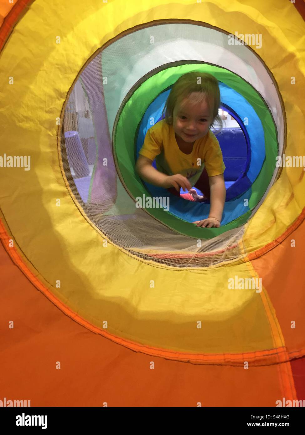 Bambina che strizza attraverso un tunnel di gioco multicolore Foto Stock