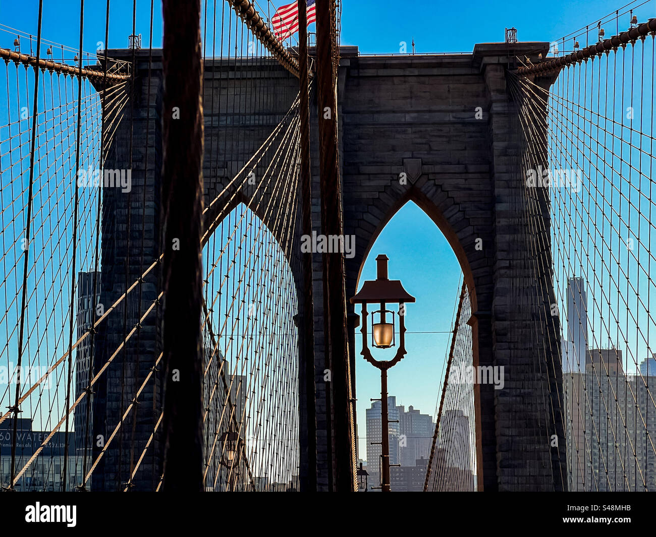 Torre di supporto, cavi sospesi e lampada del Ponte di Brooklyn contro un cielo blu brillante Foto Stock