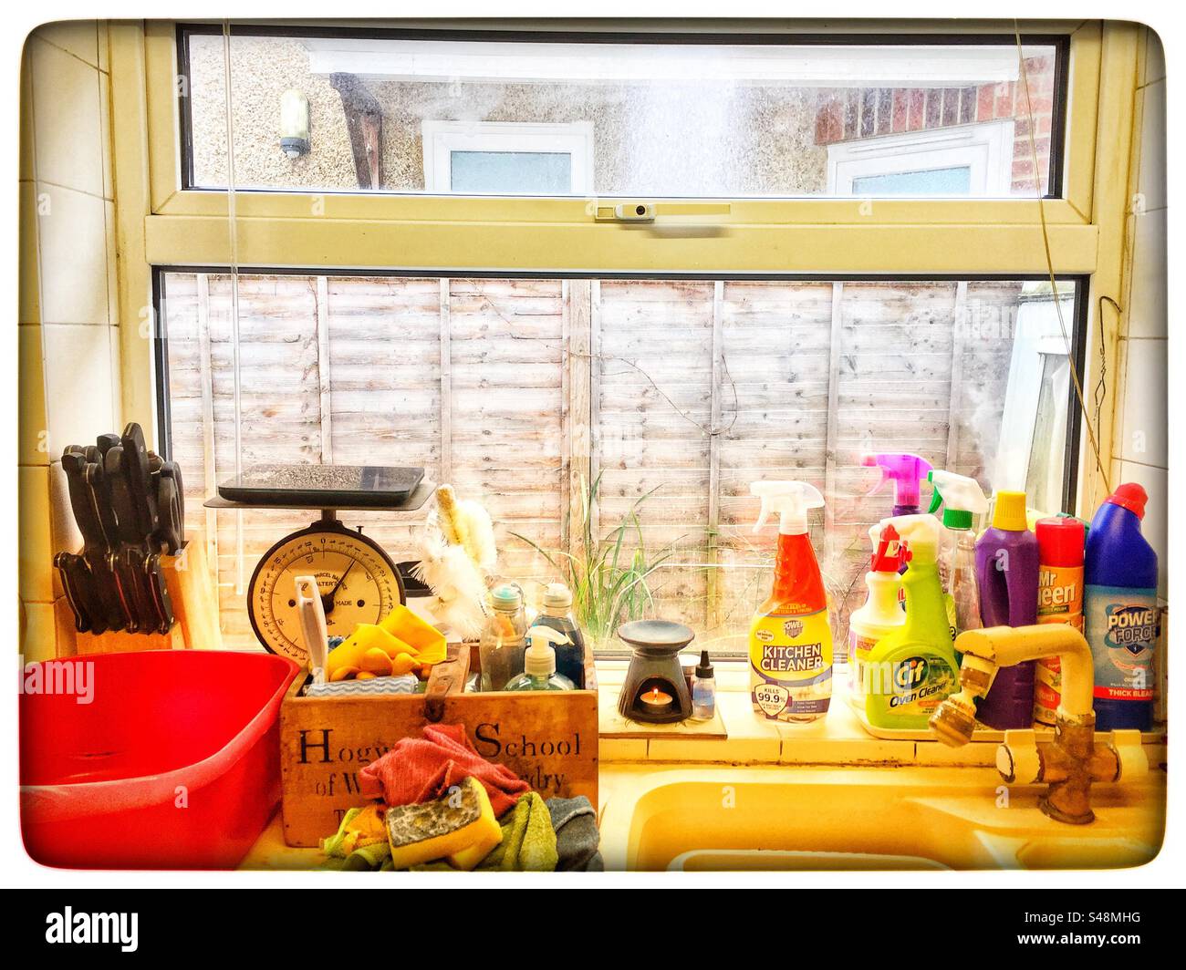Una finestra della cucina al sole del mattino con prodotti per la pulizia, pentola, bilancia a blocchi di coltelli e candela Foto Stock