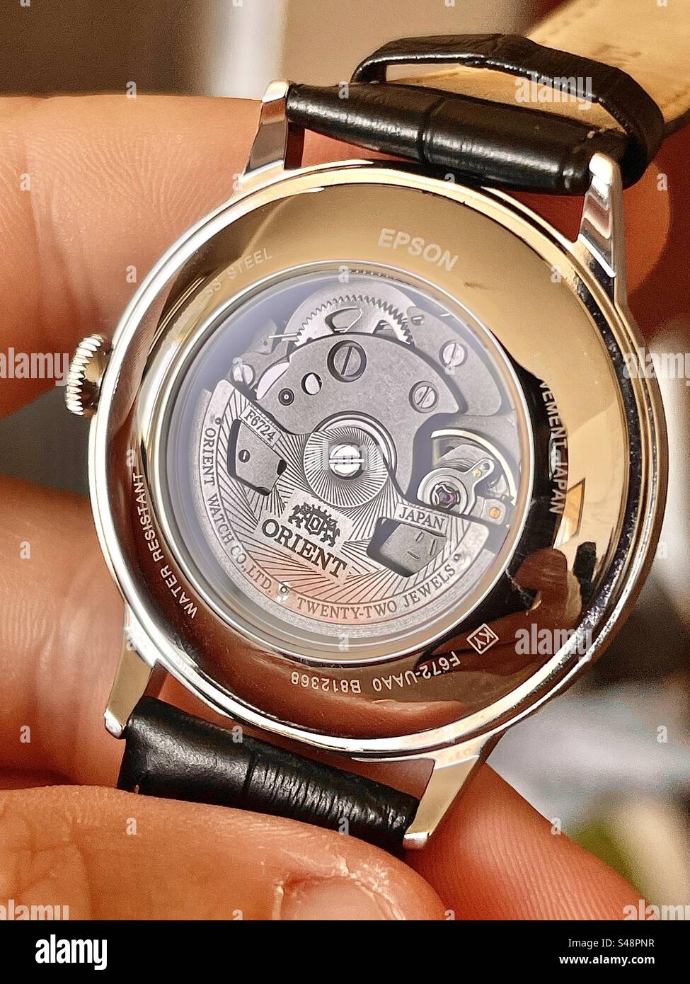 Primo piano di una mostra Back on an Orient F682-UAA0 Automatic Mechanical Watch, mostra il braccio di bilanciamento e gli ingranaggi - Immagine stock catturata con smartphone