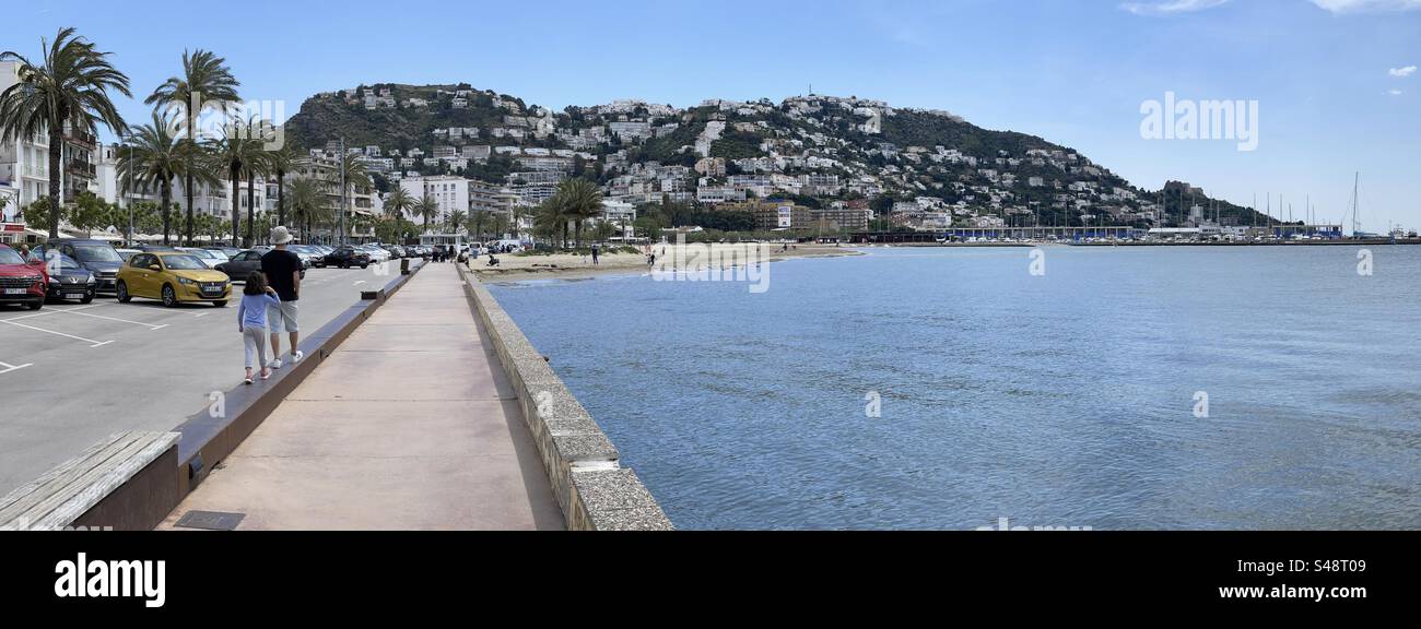 Due bambini che camminano sul lungomare con vista panoramica sul lungomare di Roses, Costa Brava, Spagna - Immagine stock catturata con smartphone