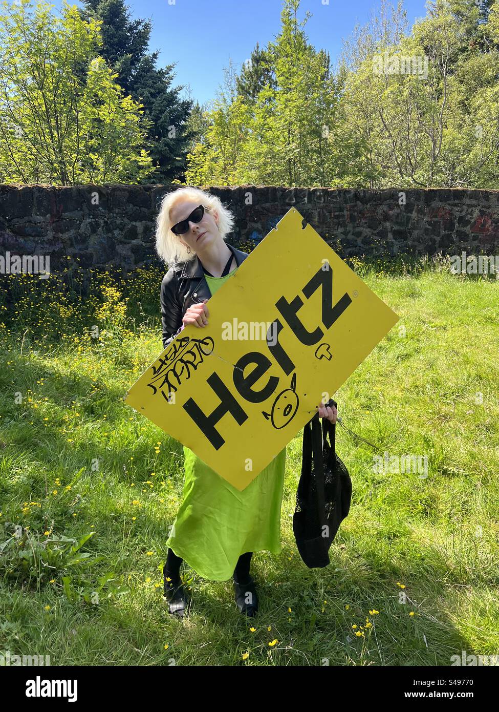 Oggetto trovato, cartellone Hertz auto a noleggio in alluminio i. Öskjuhlíð, Reykjavik. Islanda. Il cartello ha dei graffiti ed è sorretto da una signora in abito verde elettrico . Foto Stock