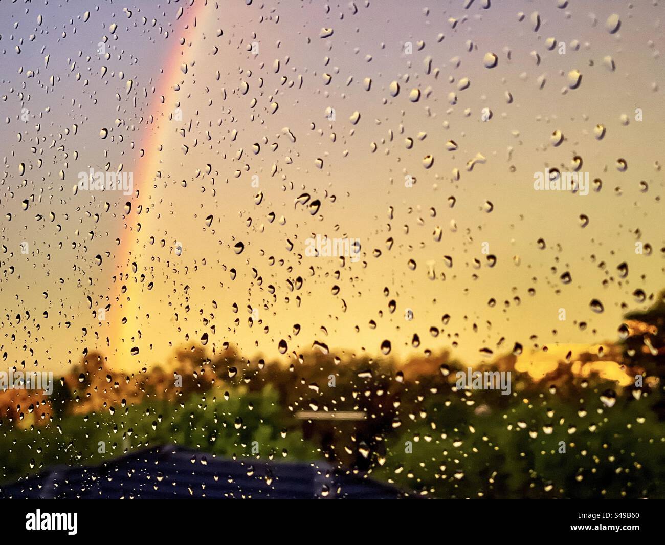 Arcobaleno nel cielo al tramonto visto attraverso le gocce di pioggia sulla finestra. Foto Stock