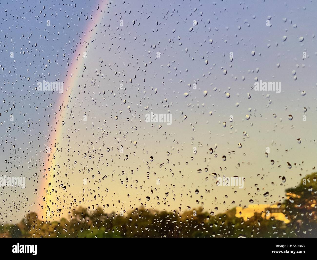 Arcobaleno nel cielo al tramonto visto attraverso le gocce di pioggia sulla finestra. Foto Stock