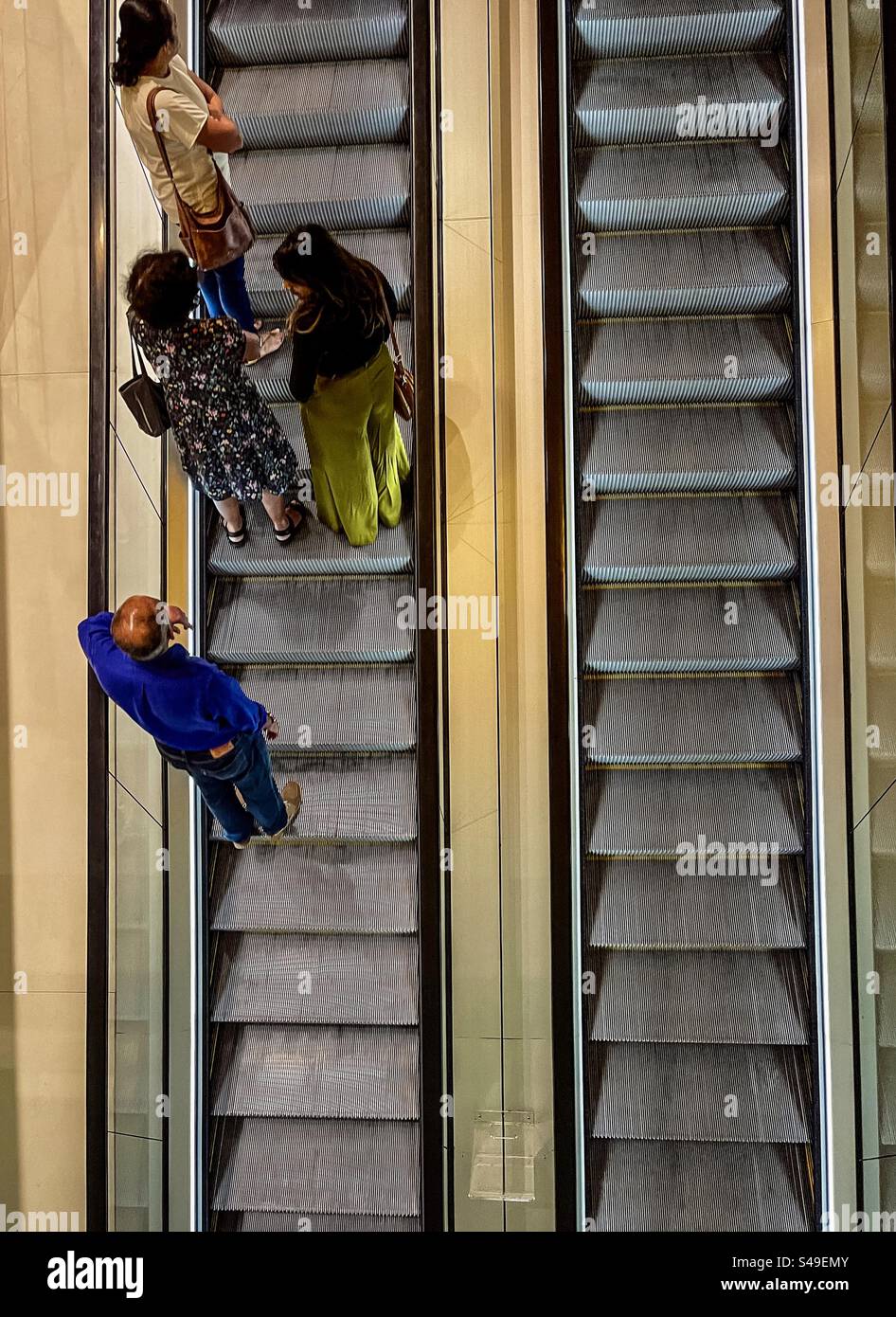 Vista ad angolo alto di due scale mobili affiancate con quattro persone in piedi su una scala mobile. Foto Stock