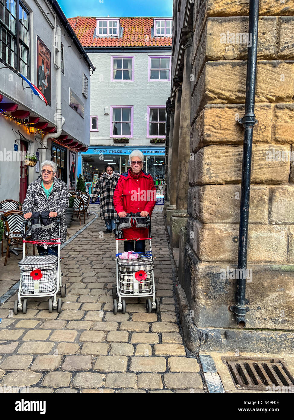 Gente anziana che cammina lungo Market Street a Whitby con i tram per lo shopping Foto Stock