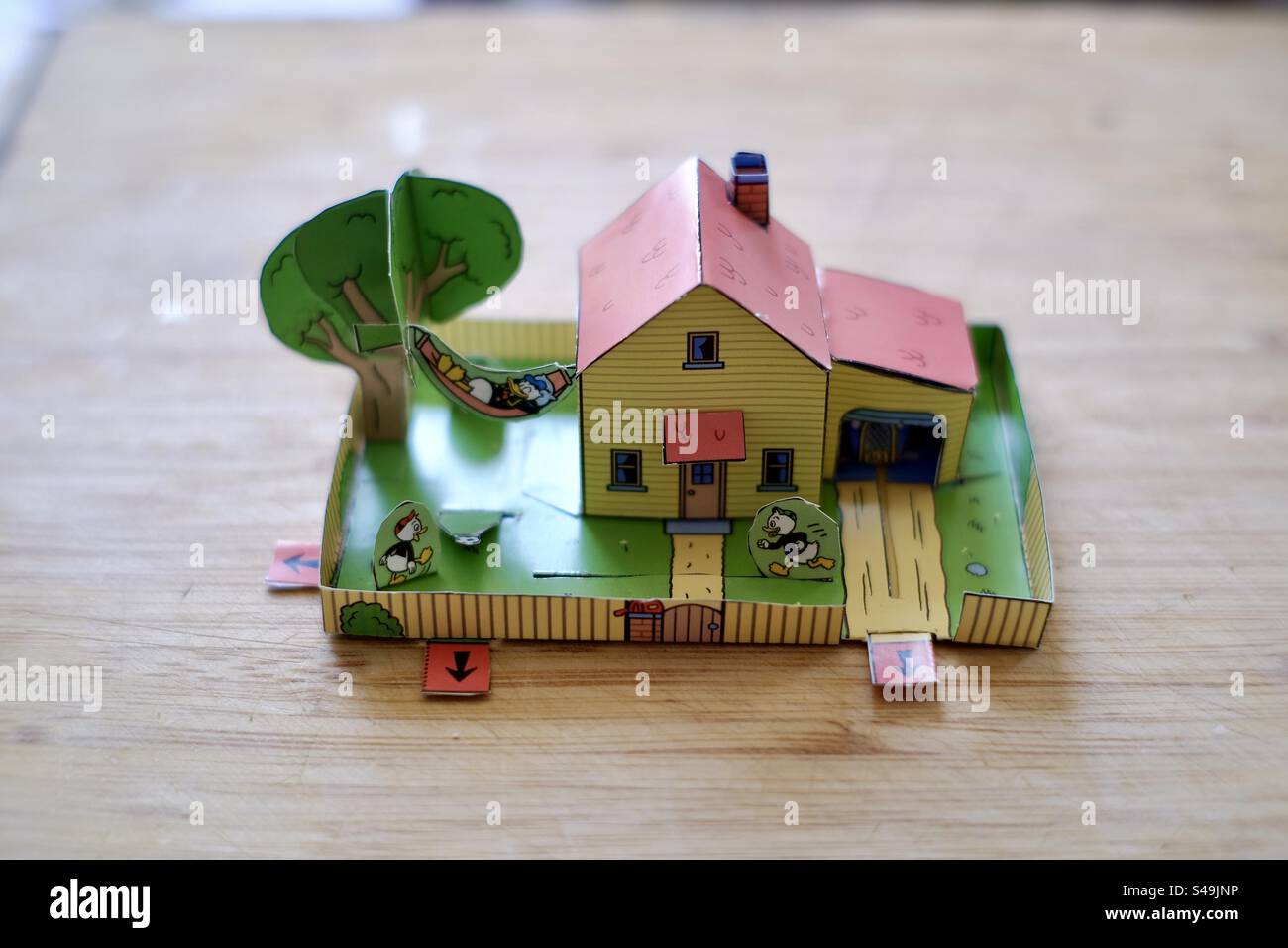 Foto ravvicinata di una casa ritagliata animata di carta o cartone e di un giardino per bambini che riposano su un tavolo di legno. Foto Stock
