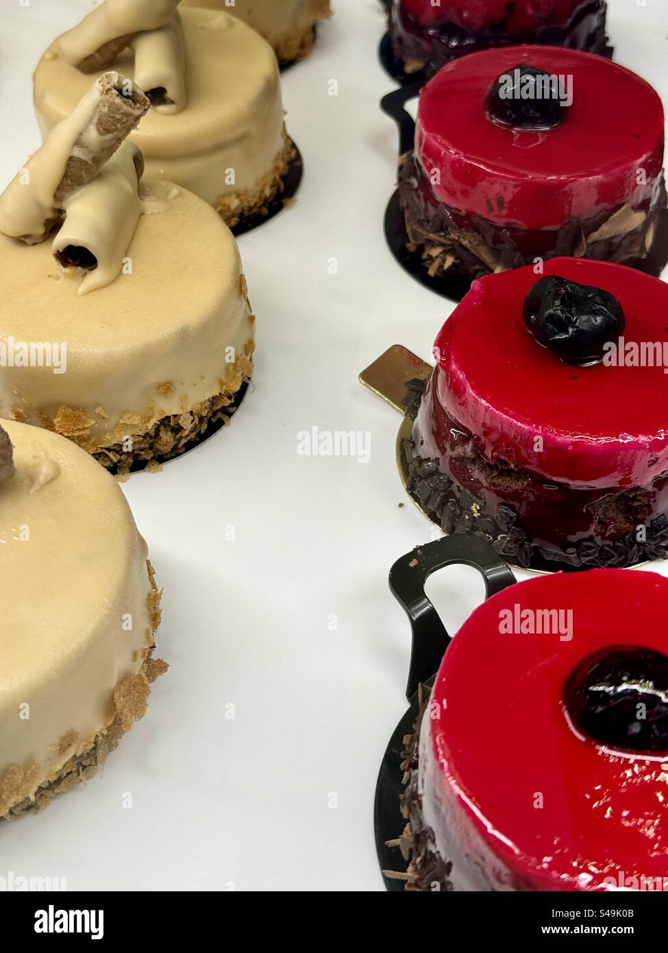 Primo piano di eleganti dolci gourmet con glassa rossa e decorazioni al cioccolato, preparati al momento in una panetteria di Atene. Foto Stock