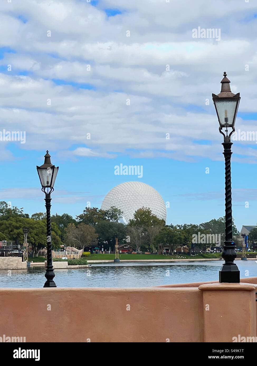 L'astronave Earth, nota anche come Epcot Ball, vista tra due lampioni attraverso Bay Lake al parco a tema Epcot a Disney World a Orlando in Florida il 1° gennaio 2024 - Immagine stock catturata con smartphone