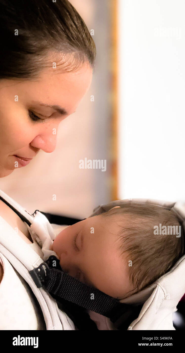 Mamma guarda il bambino che dorme nella fascia portabicchieri. Foto Stock