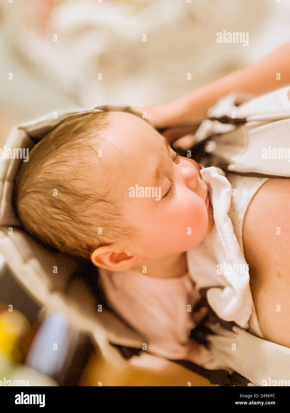 Il bambino dorme in un'imbragatura vicino al petto della madre Foto Stock