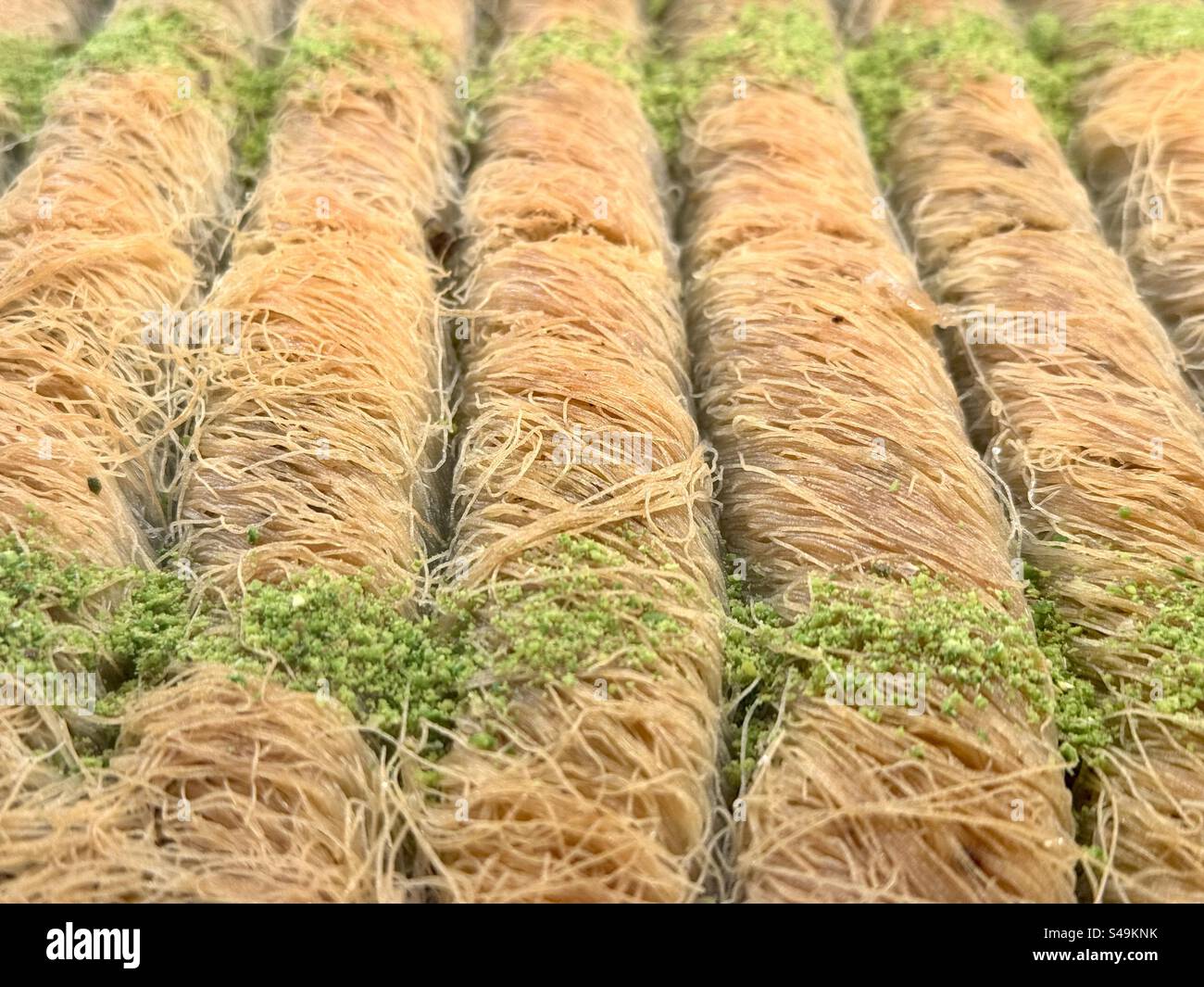Pasticcini baklava greci appena fatti disposti ordinatamente in file, luccicanti con sciroppo e conditi con pistacchi schiacciati. - Immagine stock catturata con smartphone