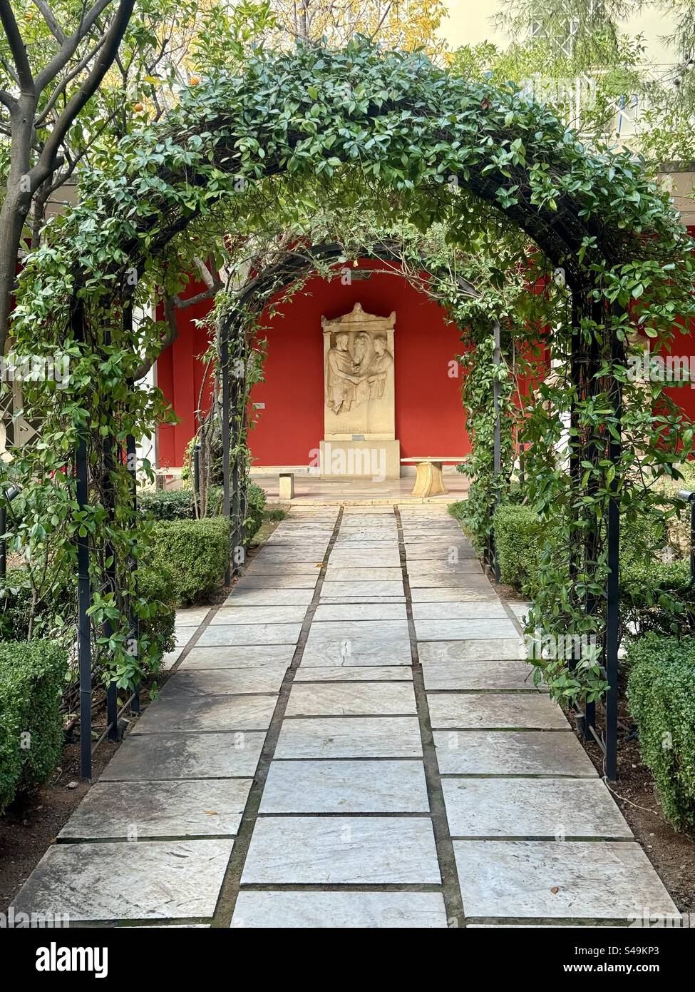 Ingresso al giardino con un arco verde e un sentiero in pietra che conduce a un monumento presso il Museo Nazionale Greco di Archeologia ad Atene, Grecia. - Immagine stock catturata con smartphone