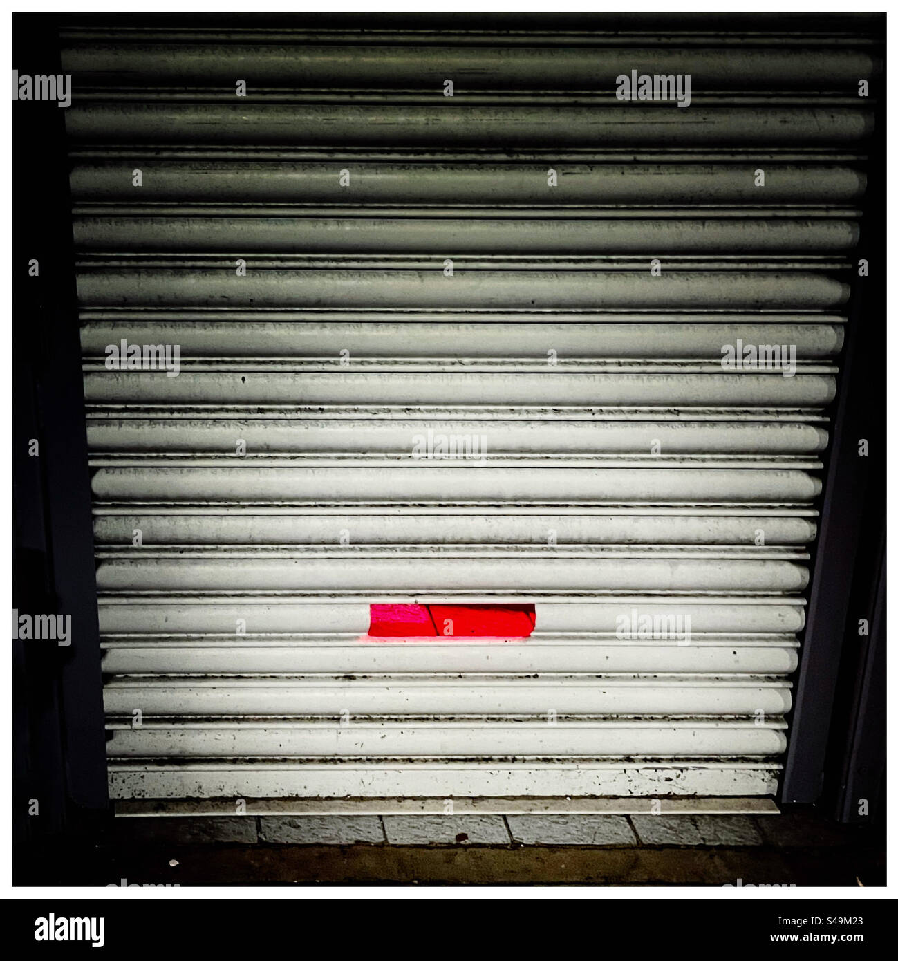 La luce rossa brilla attraverso una fessura in una porta con tapparella - Immagine stock catturata con smartphone