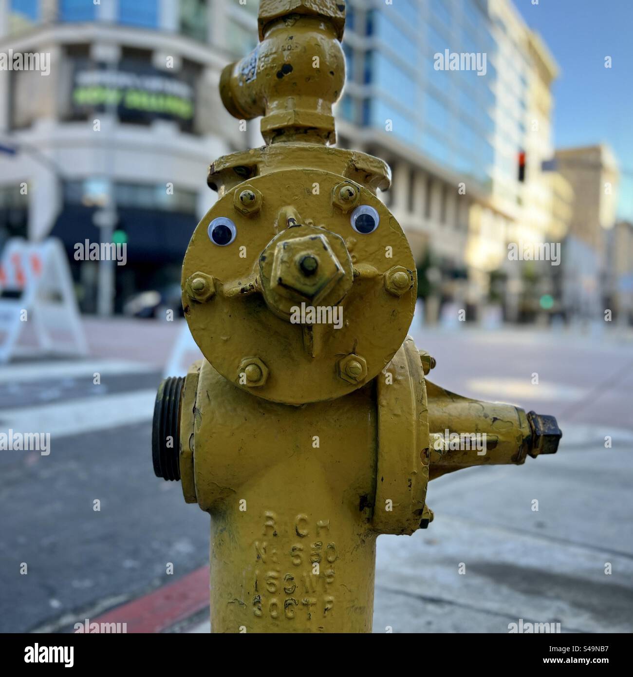 Immagine quadrata, candela di fuoco gialla (idrante) con occhi strani su un angolo di strada nel centro di Los Angeles, CA, ora del giorno - Immagine stock catturata con smartphone