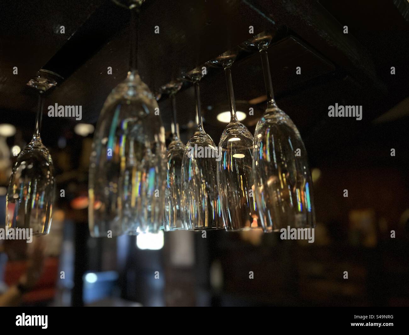 Vista a fuoco superficiale di bicchieri da champagne puliti e scintillanti appesi a un rack in un bar, sfondo scuro Foto Stock