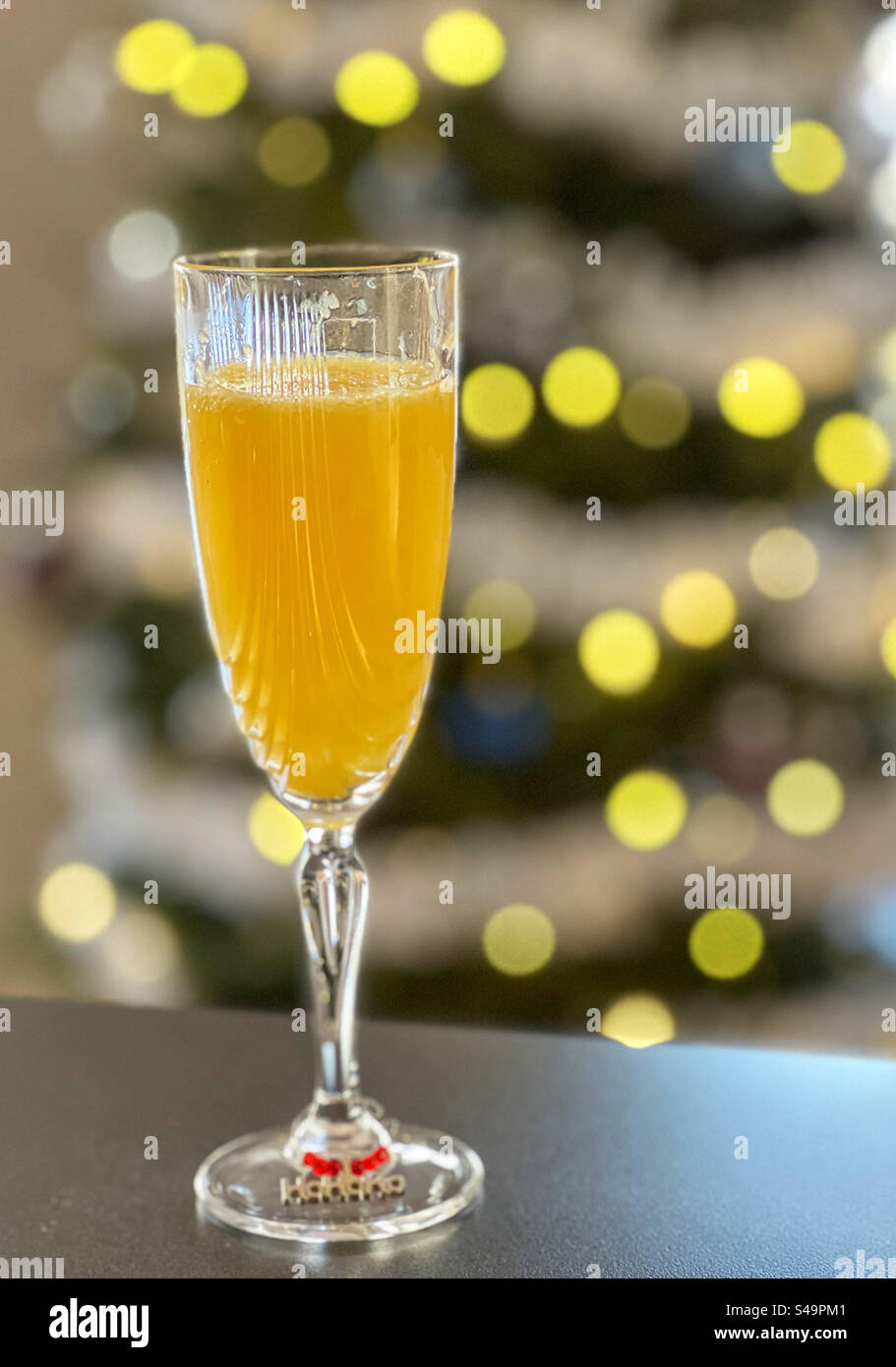 Bicchiere di champagne con Bucks Fizz o cocktail mimosa, con bokeh di luci dell'albero di Natale sullo sfondo. Foto Stock