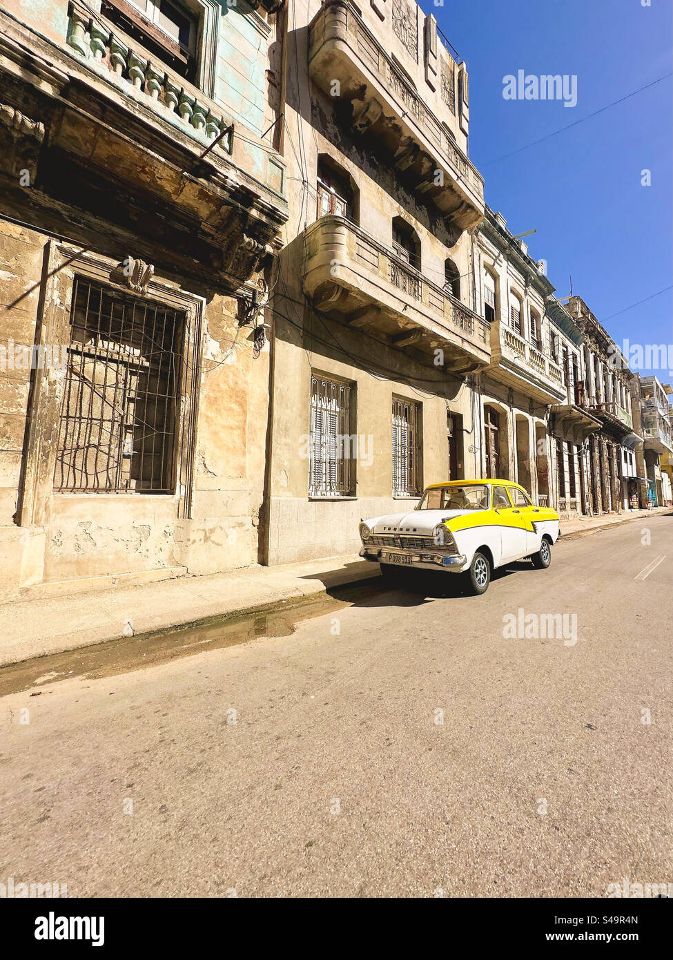 Facciate di edifici trascurati a l'Avana. Una vecchia auto d'epoca parcheggiata davanti. L'Avana, Cuba Foto Stock