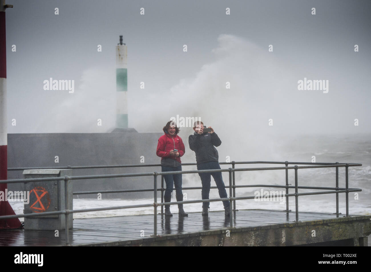 Aberystwyth Regno Unito 16/03/2019 UK meteo: Le persone hanno difficoltà a camminare come Storm Hannah offre enormi onde che si infrangono nel faro del porto e le difese del mare su un estremamente bagnato e ventoso giorno in Aberystwyth Wales. Raffiche di oltre 50mph sono previsioni di impatto delle parti il nord e l ovest del paese oggi come il periodo di molto le perturbazioni atmosferiche continua a dominare il Regno Unito Photo credit: Keith Morris/Alamy Live News Foto Stock