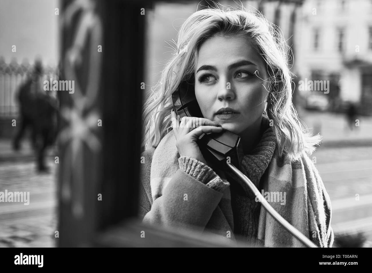 Giovane bella donna bionda facendo una chiamata importante in un vintage telefono pubblico booth su una soleggiata sera Foto Stock