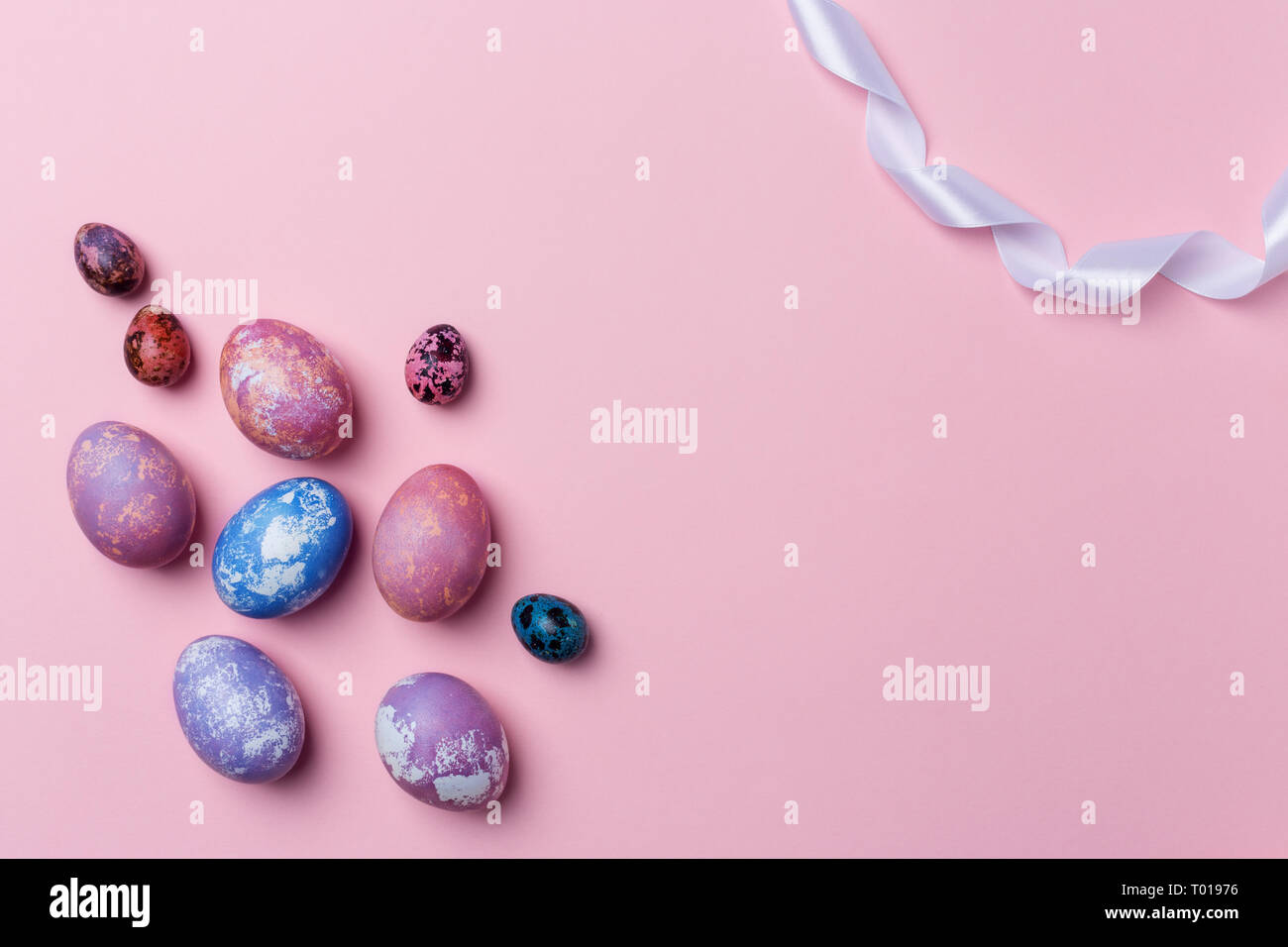 Uova colorate e uova di quaglia con nastro bianco su sfondo rosa, copia del telaio dello spazio. Cibo sano concetto. Vista superiore, piatto laici. Uova di Pasqua. Felice Est Foto Stock