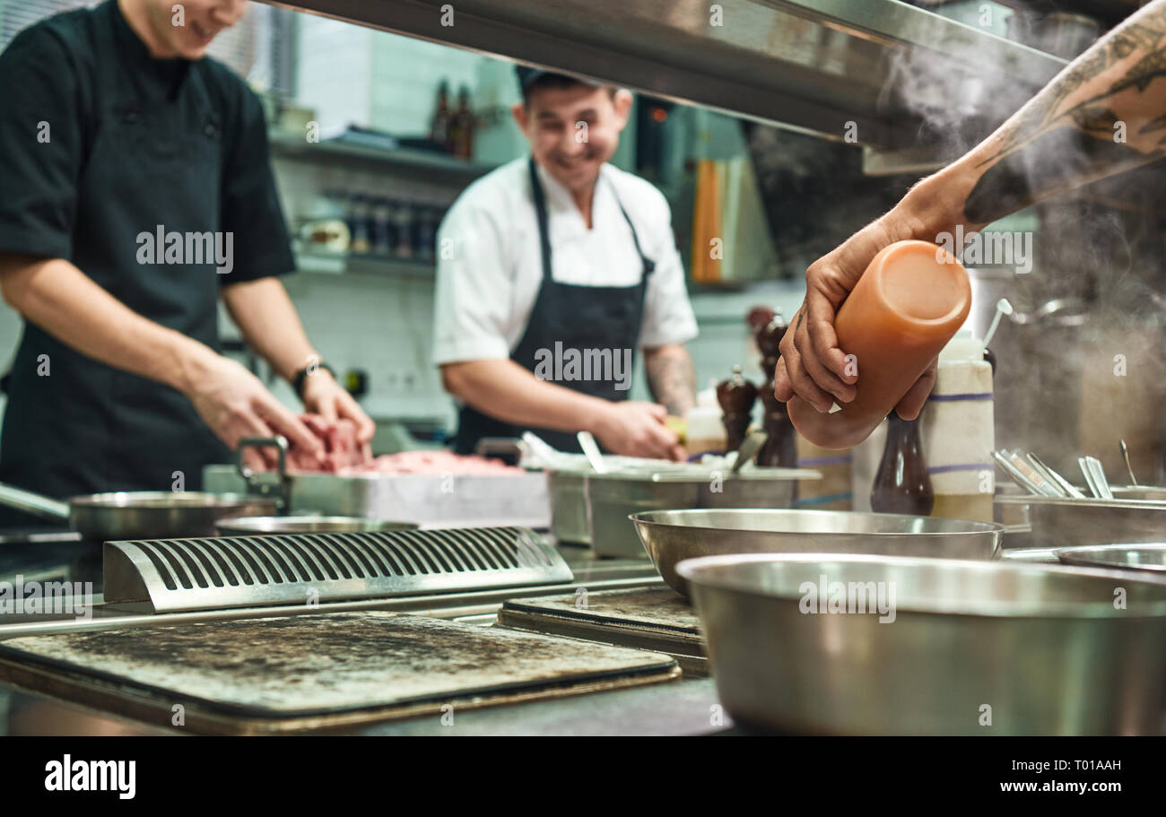 Team di Professionisti. Allegro giovani cuochi preparare il cibo insieme in un ristorante di cucina. Concetto di cucina a vista Foto Stock