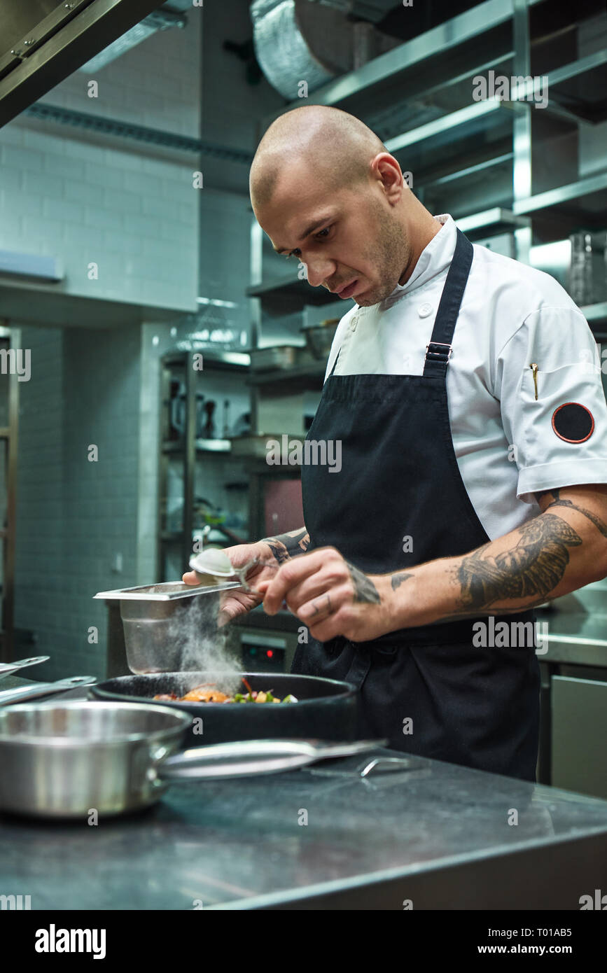 Hai bisogno di più di spezie. Foto verticale del ristorante lo chef con parecchi tatuaggi aggiungendo una speciale di spezie fresche cucinate la pasta alla carbonara. Il cibo italiano Foto Stock