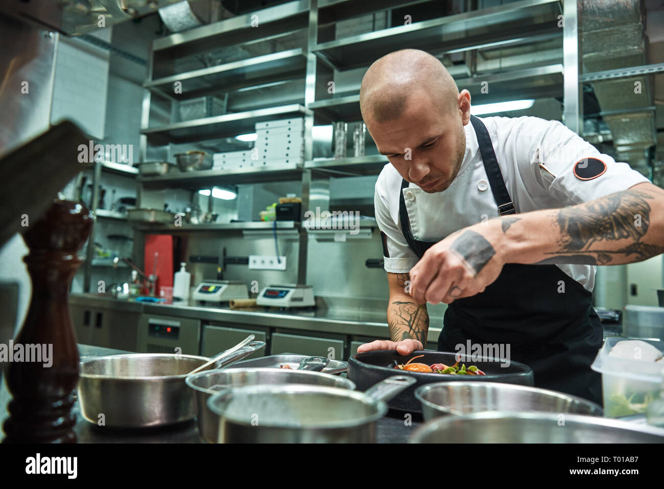 Delicato lavoro. Famosi chef fiducioso con parecchi tatuaggi sui suoi bracci di guarnitura Carbonara di pasta in un ristorante di cucina. Concetto di cibo Foto Stock