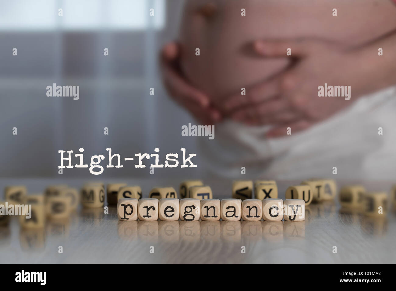 Parole ad alto rischio di gravidanza composto da lettere di legno. Donna incinta in background Foto Stock