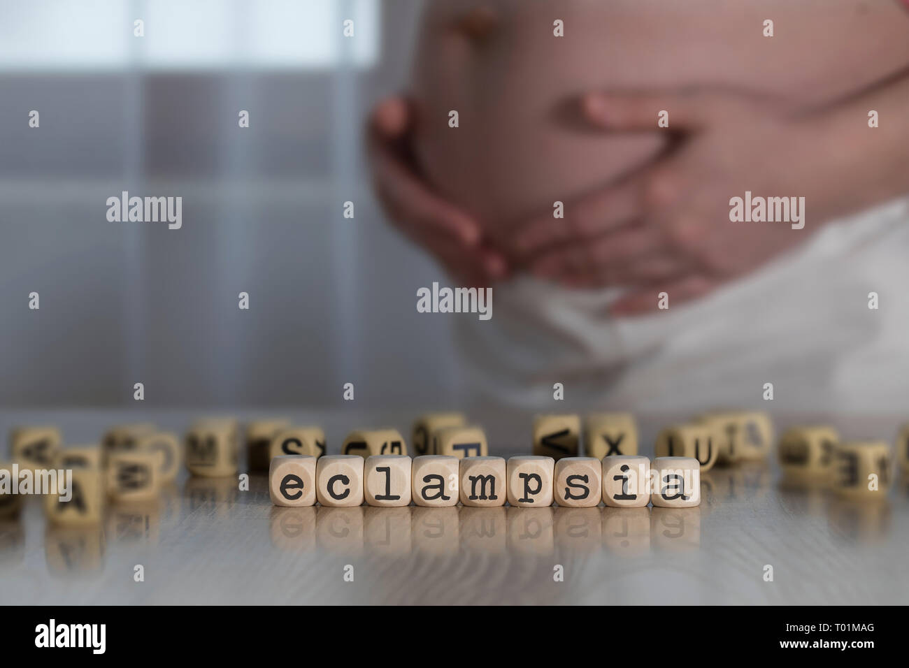Parola ECLAMPSIA composto da lettere di legno. Donna incinta in background Foto Stock